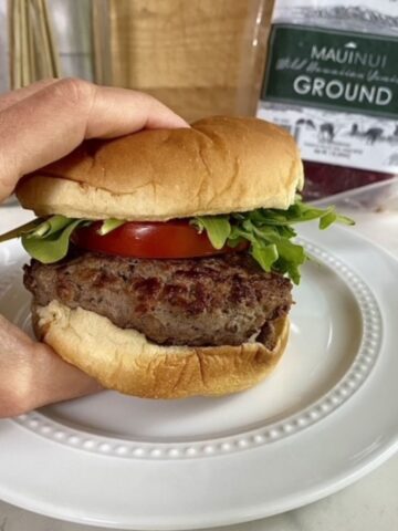 A cooked Venison Burger on a bun with arugula and tomato.