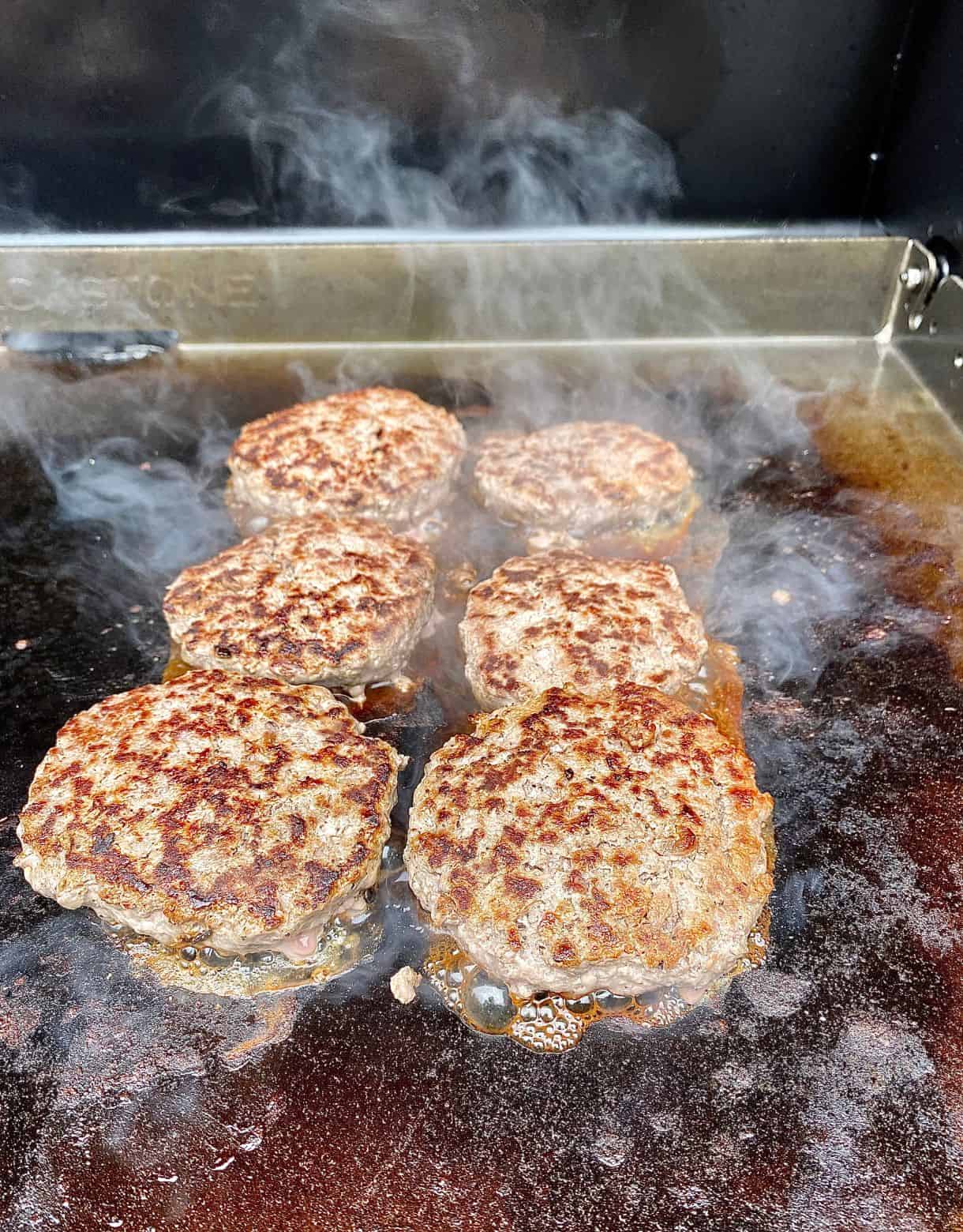 Venison burgers on a grill with steam coming off.