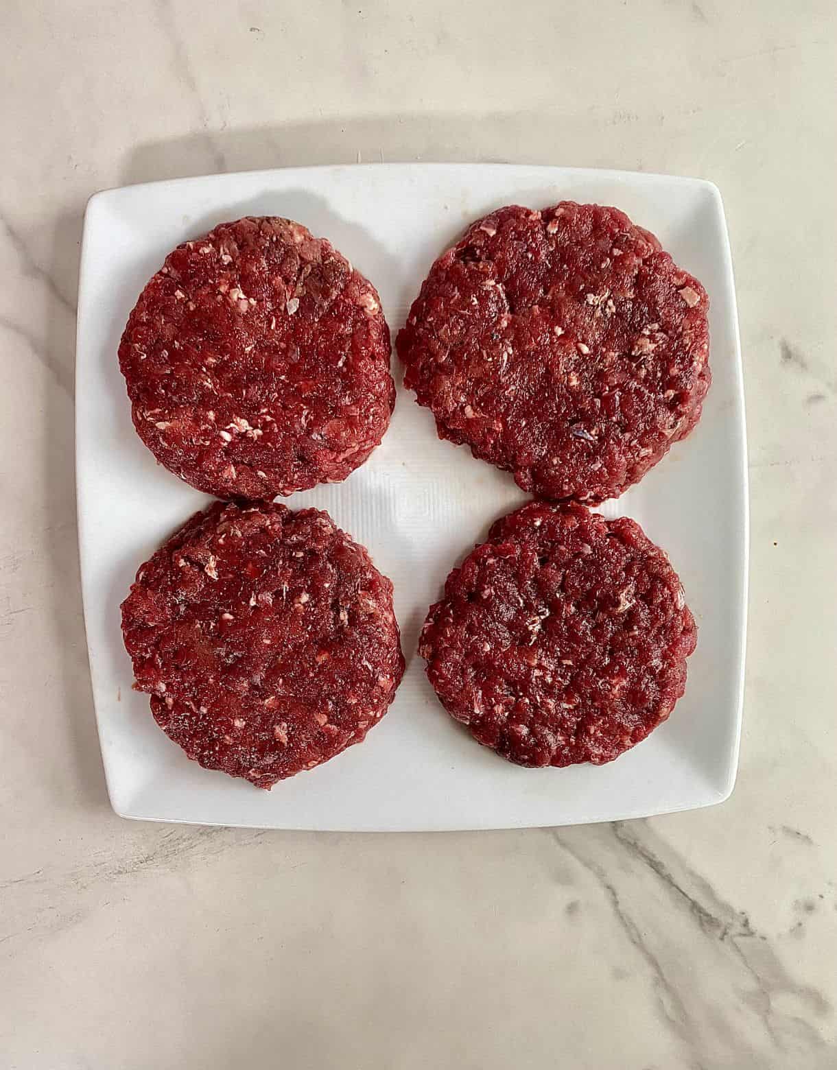 Four raw venison burger patties on a plate.