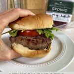 A cooked Venison Burger on a bun with arugula and tomato.