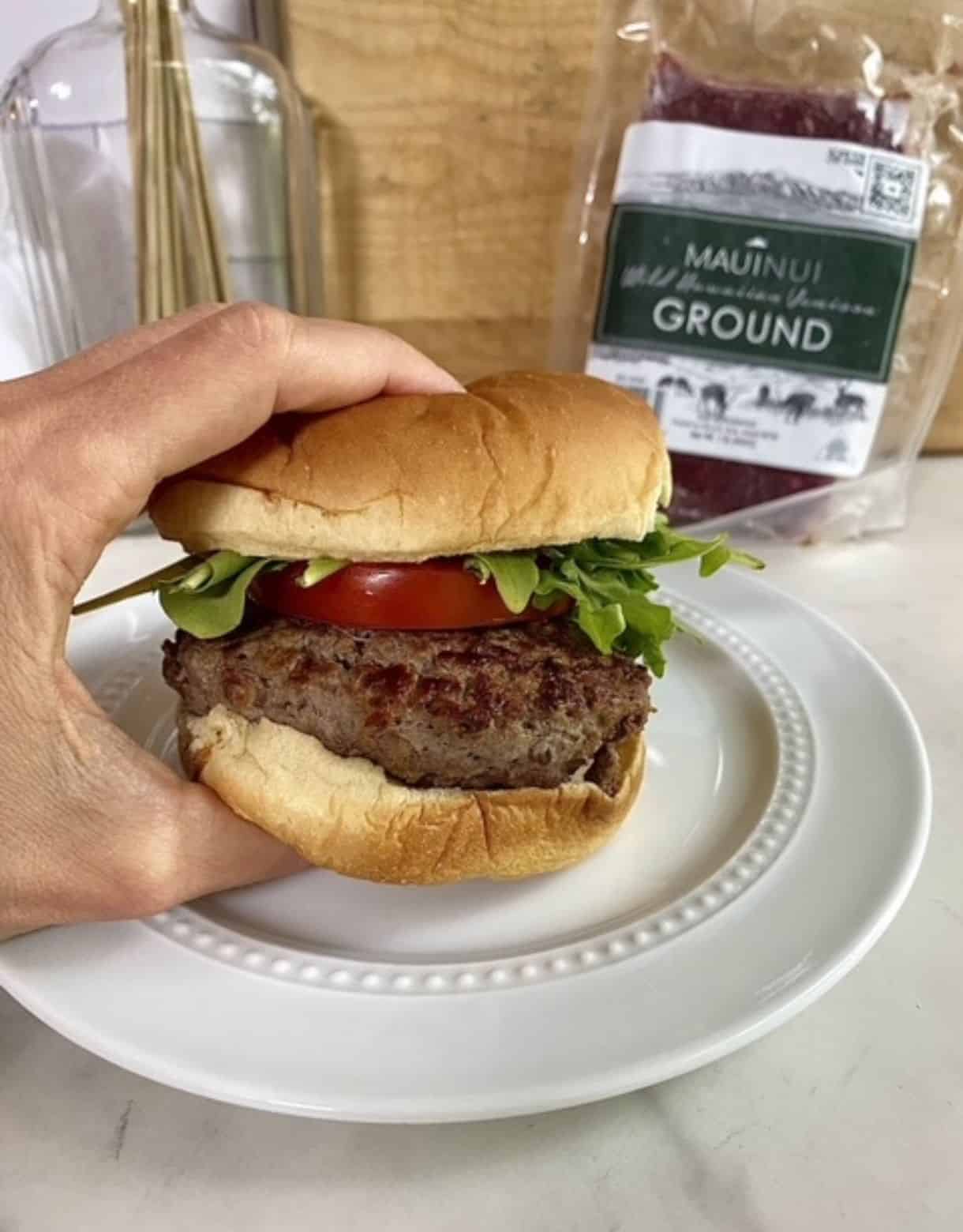 A cooked Venison Burger on a bun with arugula and tomato.