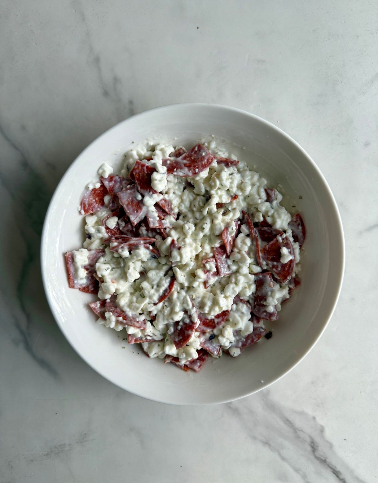 A bowl with cottage cheese mixed with spices and chopped pepperoni.