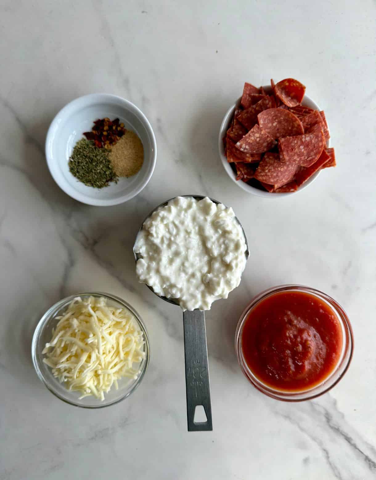 Small containers of ingredients including cottage cheese, pepperoni, marinara sauce, shredded mozzarella cheese and spices.