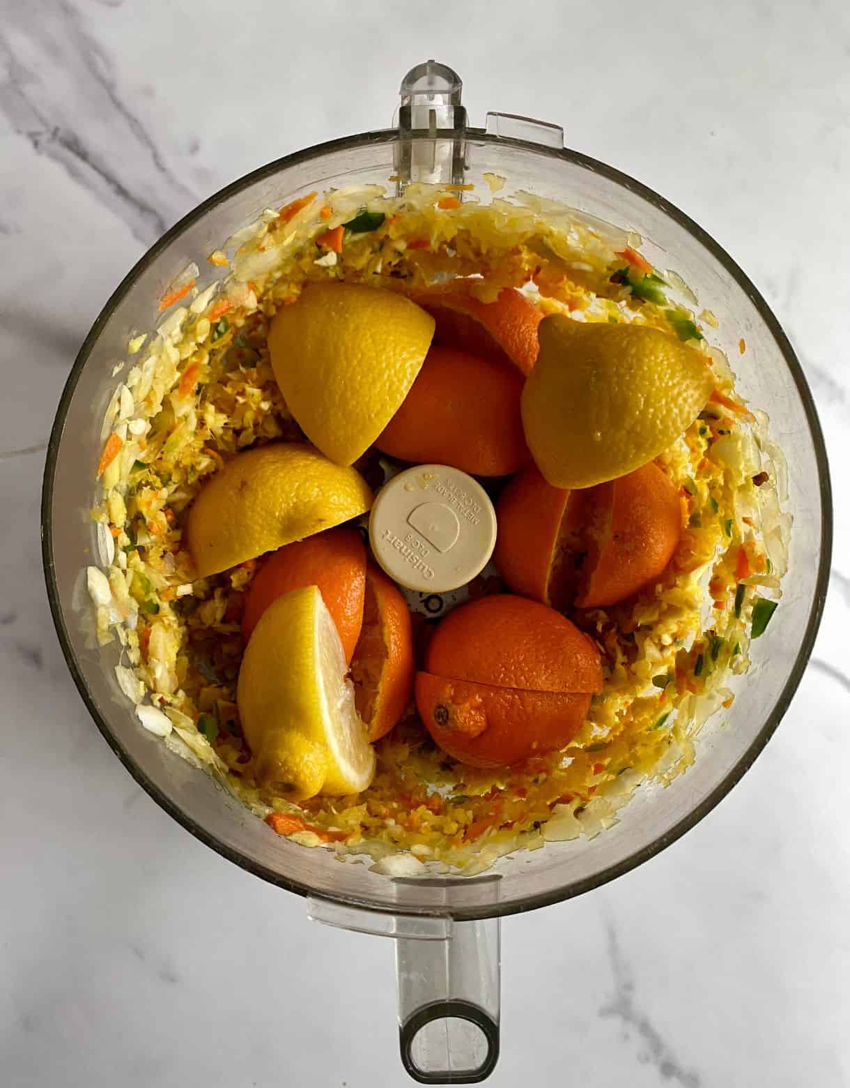 a food processor with pulverized onion, jalapenos, lemon, oranges, garlic, turmeric root, ginger root and horseradish root.
