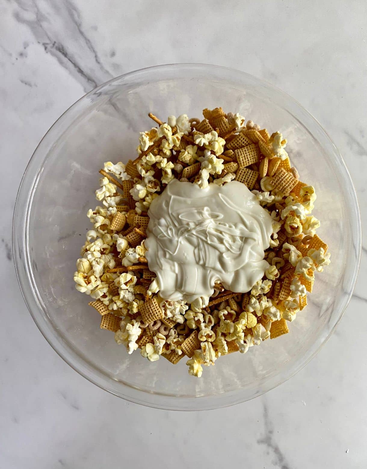 A bowl of snack mix with melted white chocolate poured on top.