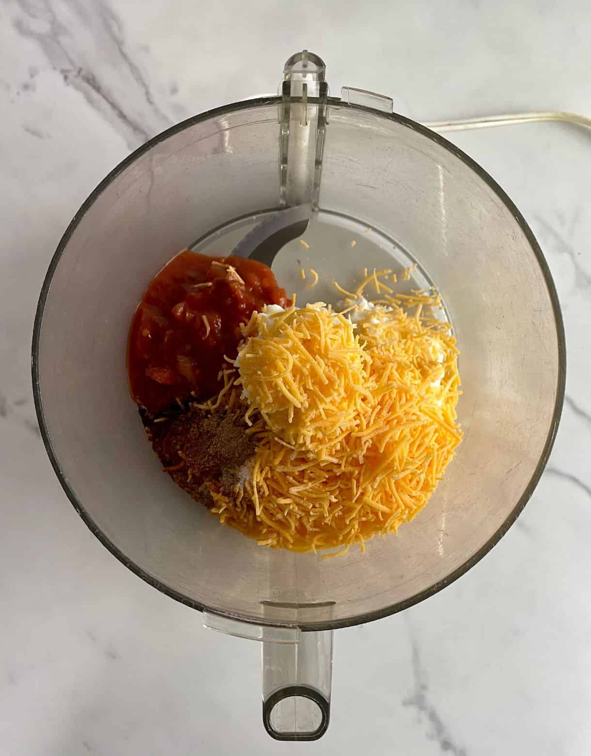 A food processor with cottage cheese, cheddar cheese, salsa and spices added but not mixed.