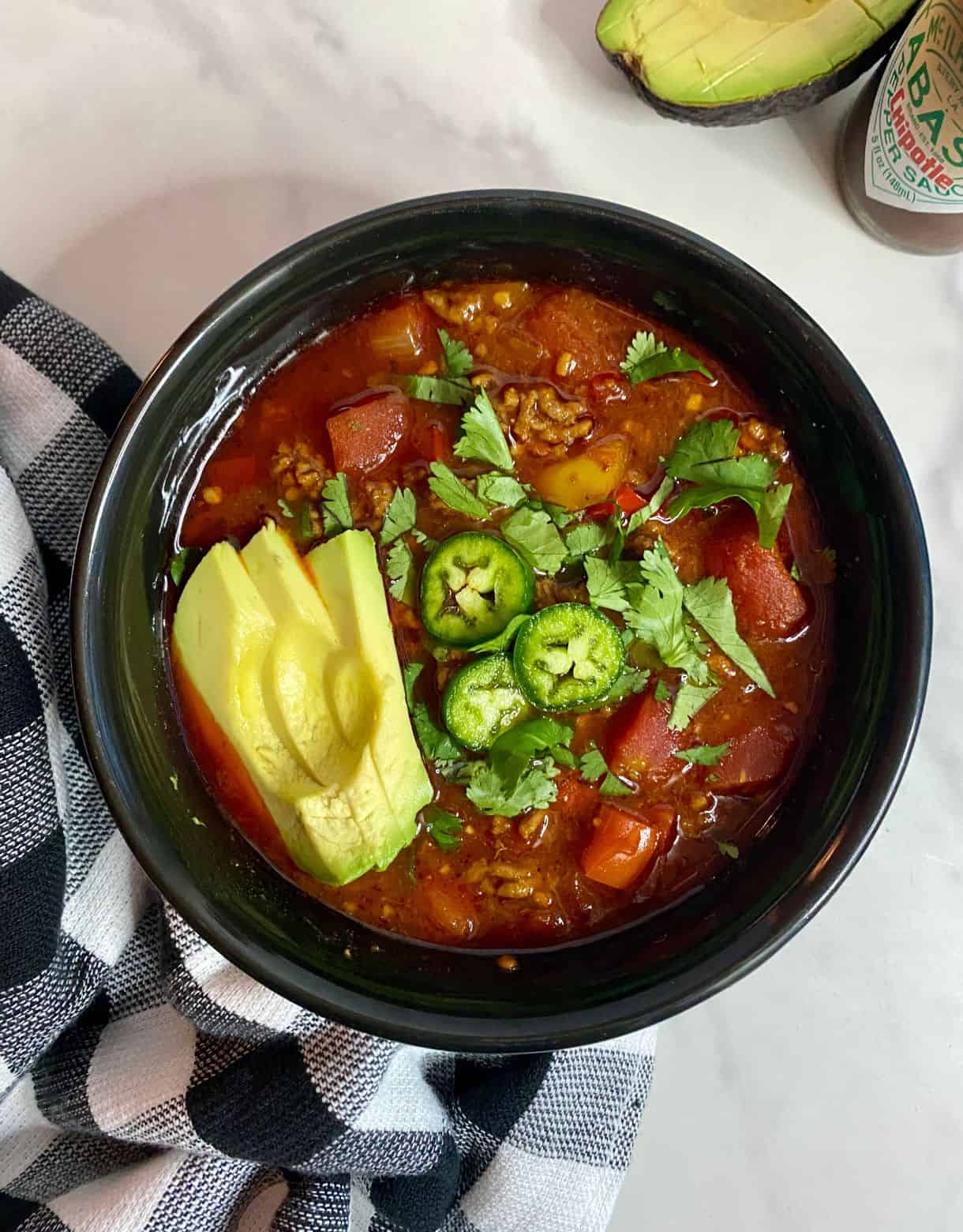 A bowl of cooked Slow Cooker Venison Chili topped with sliced avocado, chopped cilantro and sliced jalapenos.