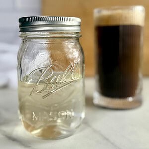 A jar of Sugar-Free Simple Syrup with a cup of coffee in the background.