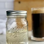 A jar of Sugar-Free Simple Syrup with a cup of coffee in the background.