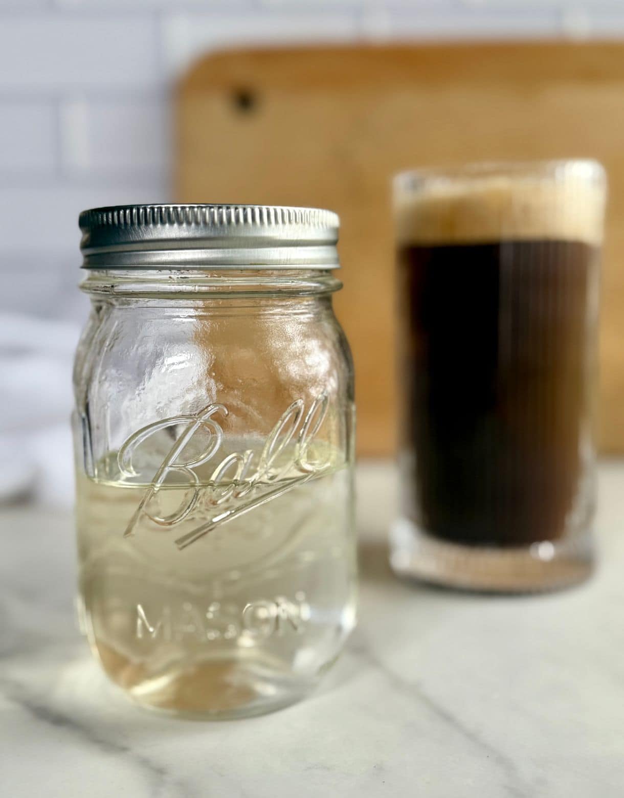 A jar of Sugar-Free Simple Syrup with a cup of coffee in the background.
